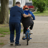 A foster dad teaching a boy how to ride a bike